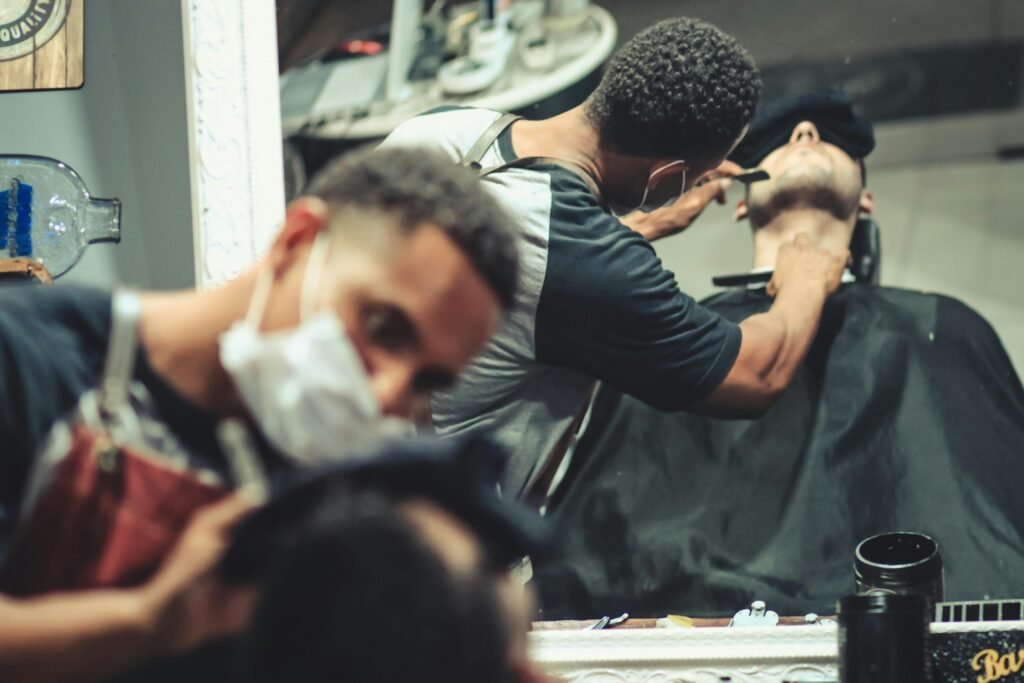 A barber wearing a face mask shaves a client in a stylish shop.