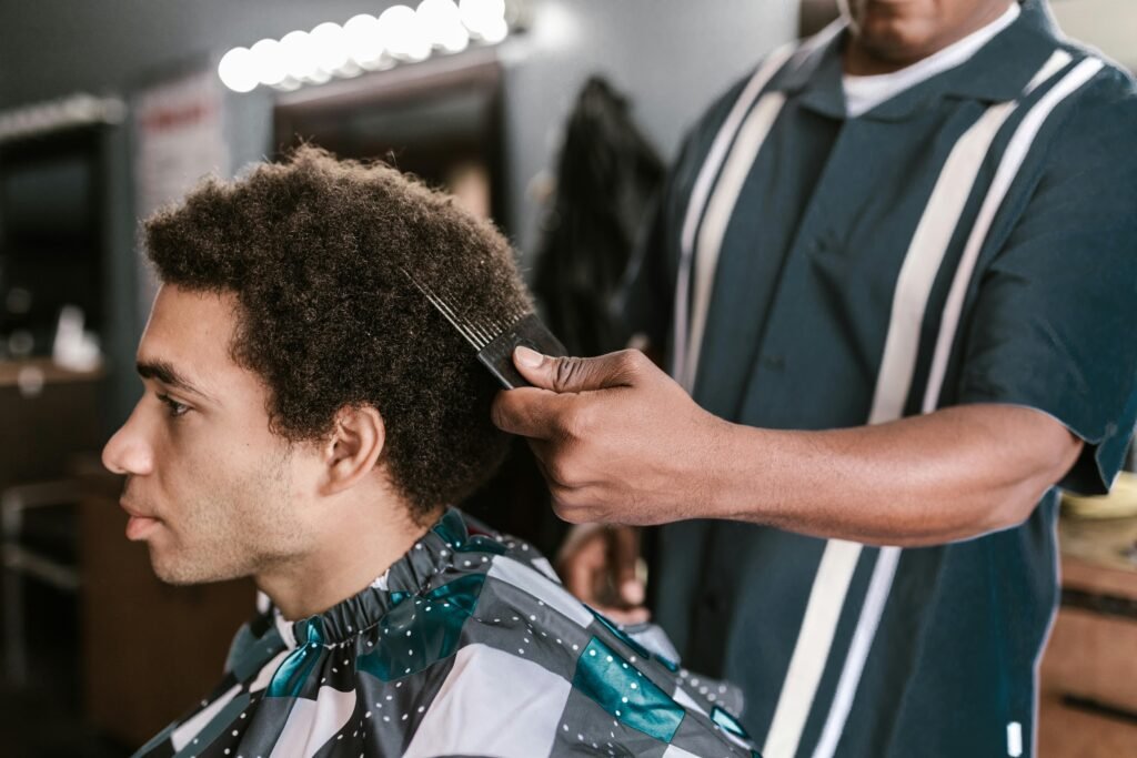 A barber uses an afro pick to style a client's hair in a modern barbershop setting.